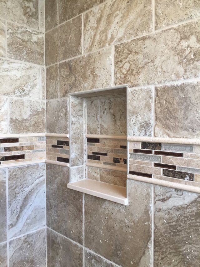 A shower with a tiled wall and a shelf in the corner.