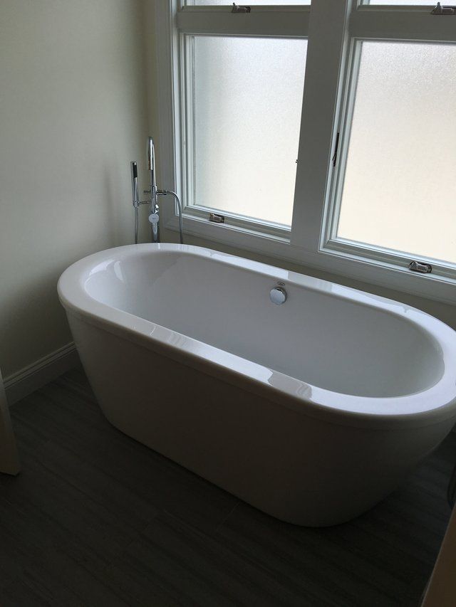 A white bathtub in a bathroom next to a window