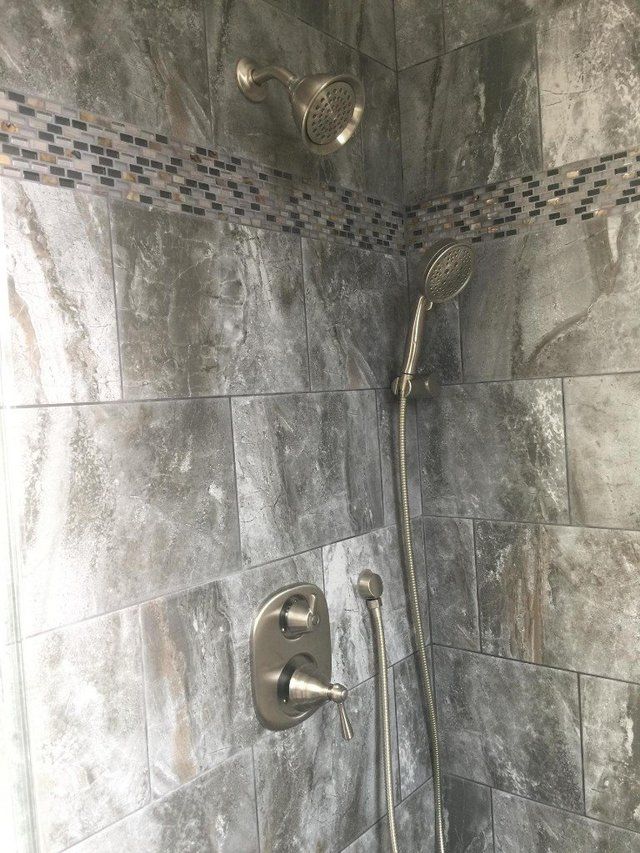 A shower with gray tiles and a stainless steel shower head.