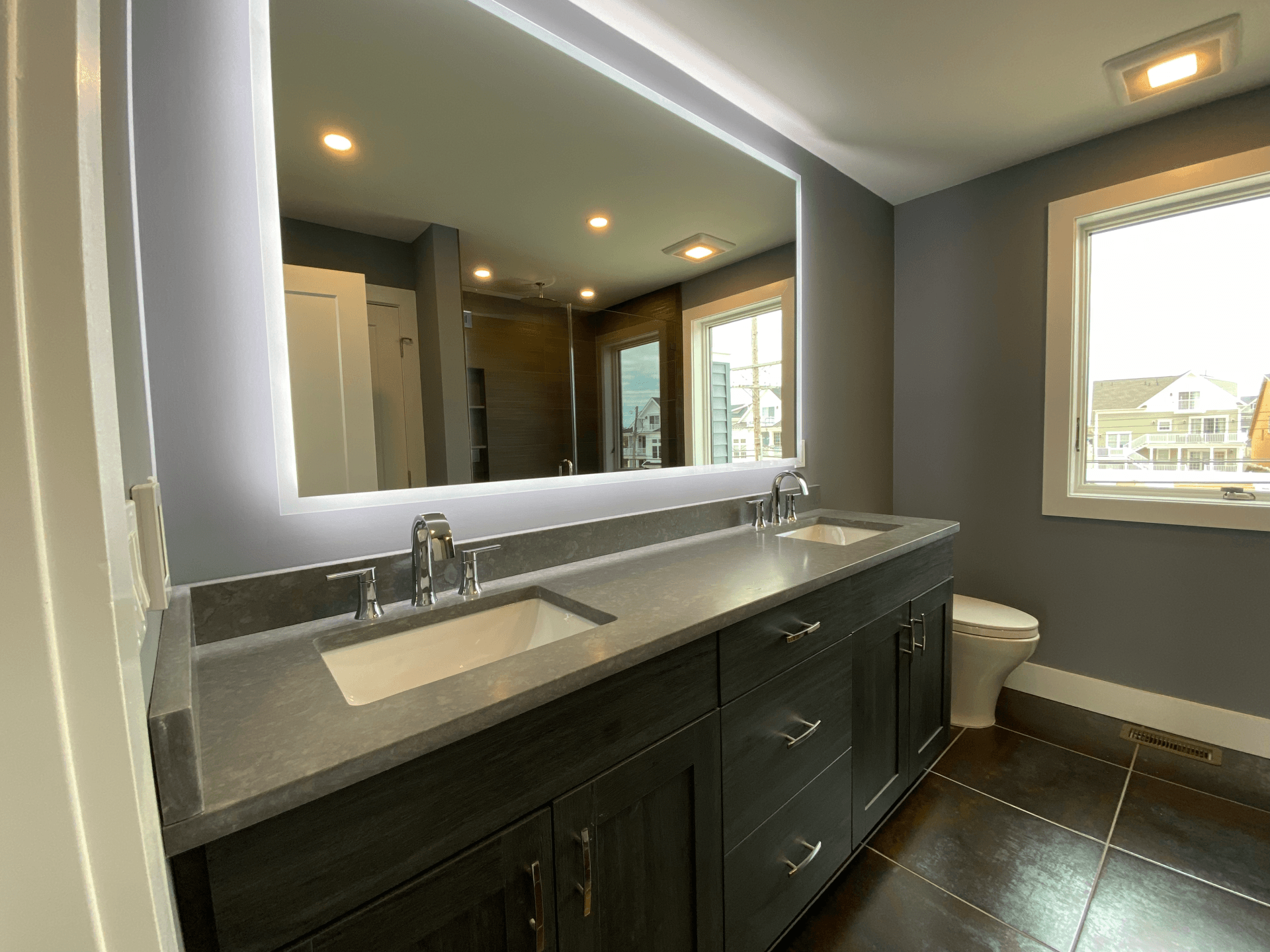 A bathroom with two sinks , a toilet and a large mirror.