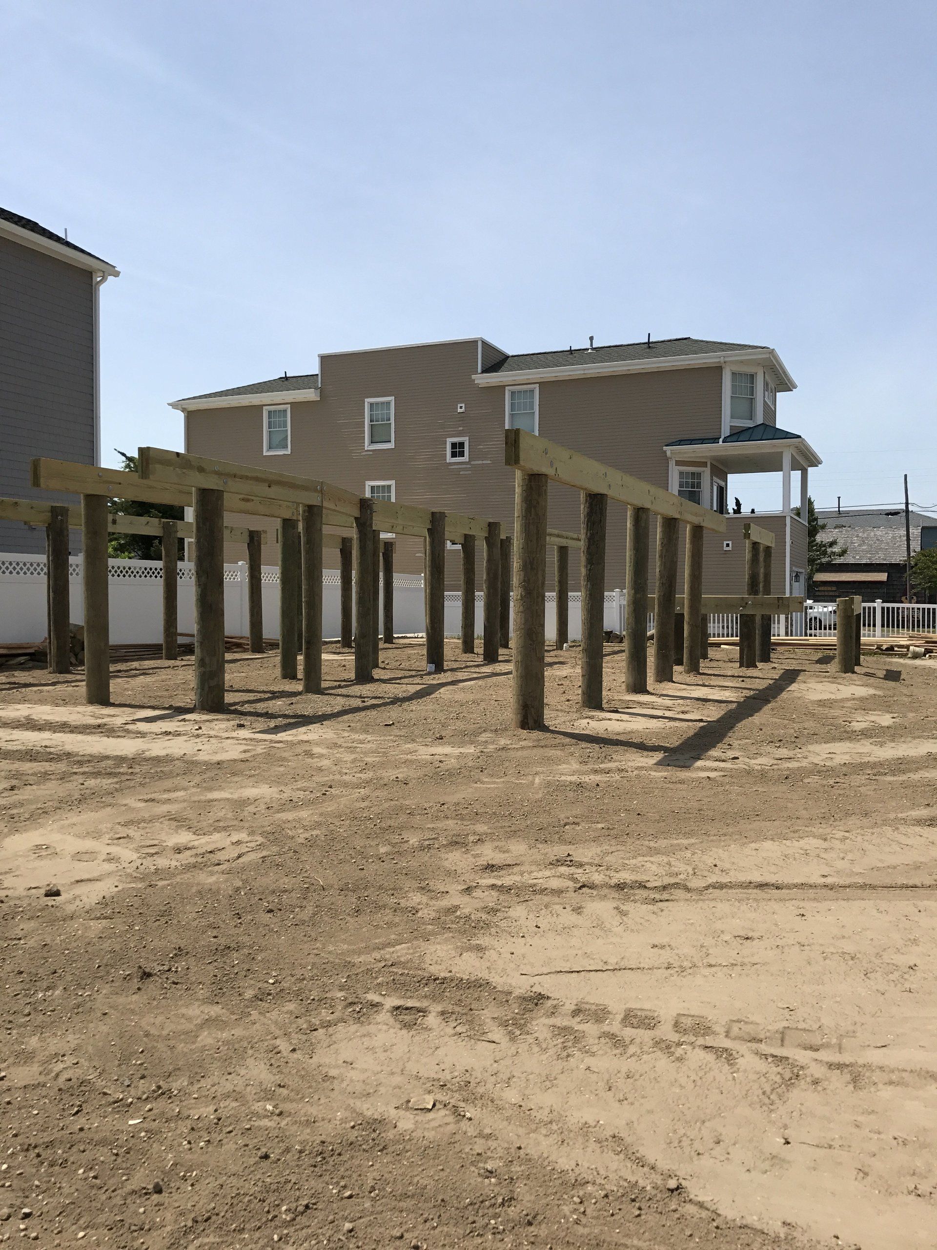 A row of wooden posts in a dirt field with a house in the background.