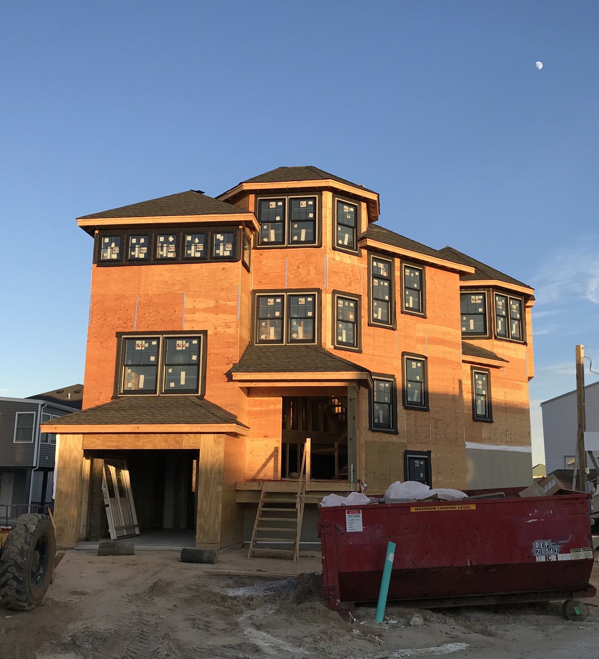 A large brick house under construction with a red dumpster in front of it