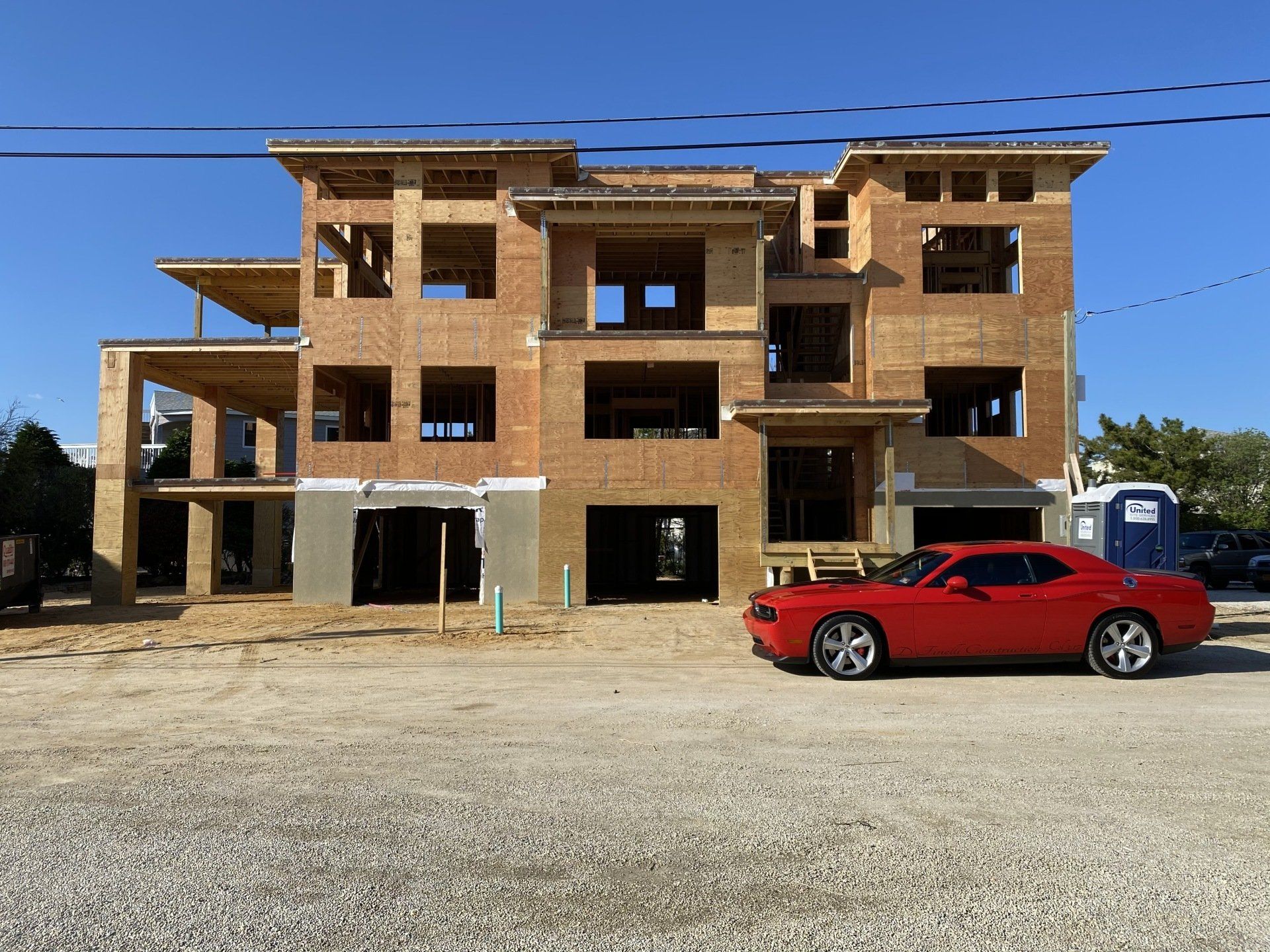 A red car is parked in front of a building under construction.