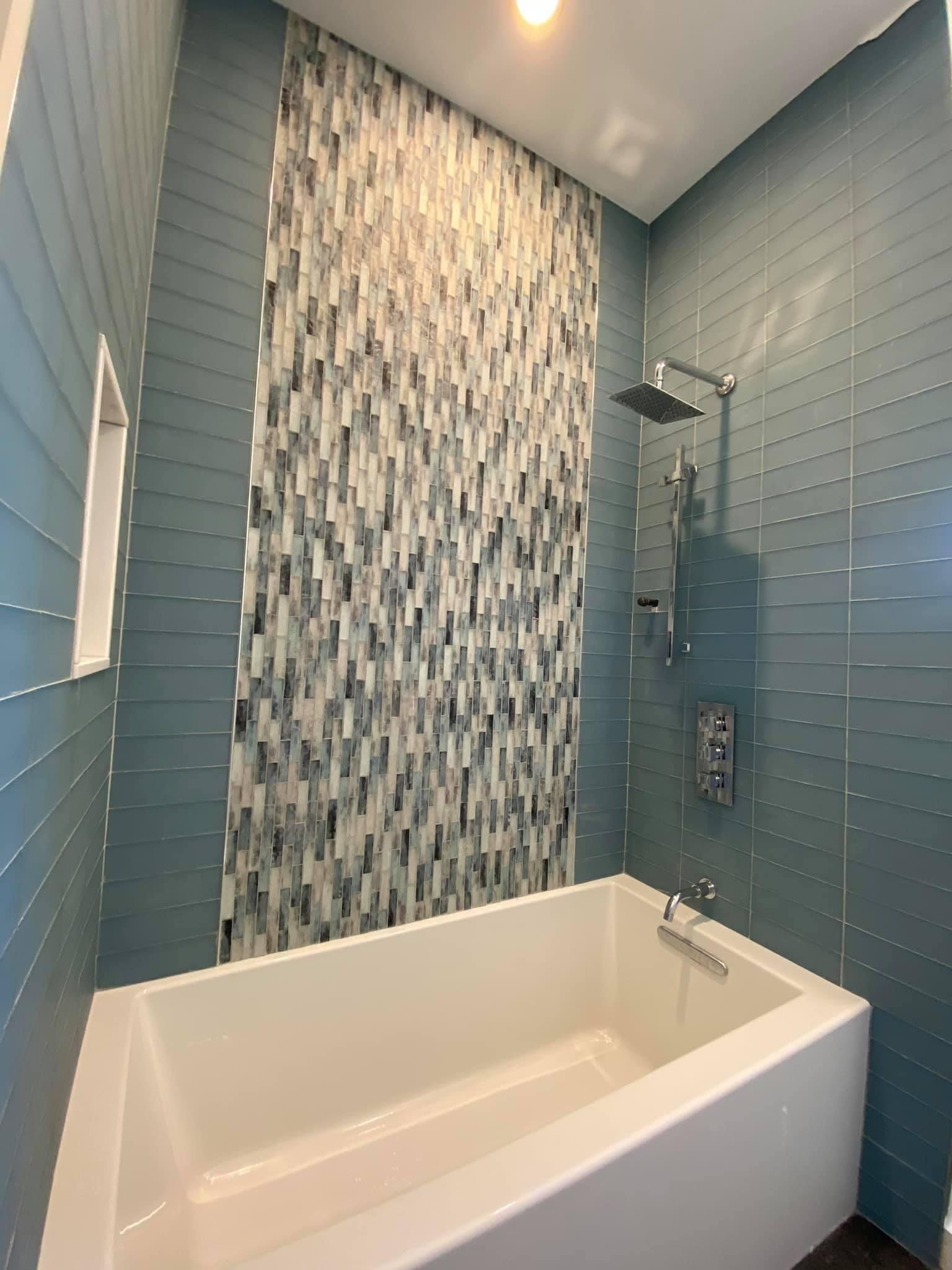 A bathtub in a bathroom with blue tiles and a shower.