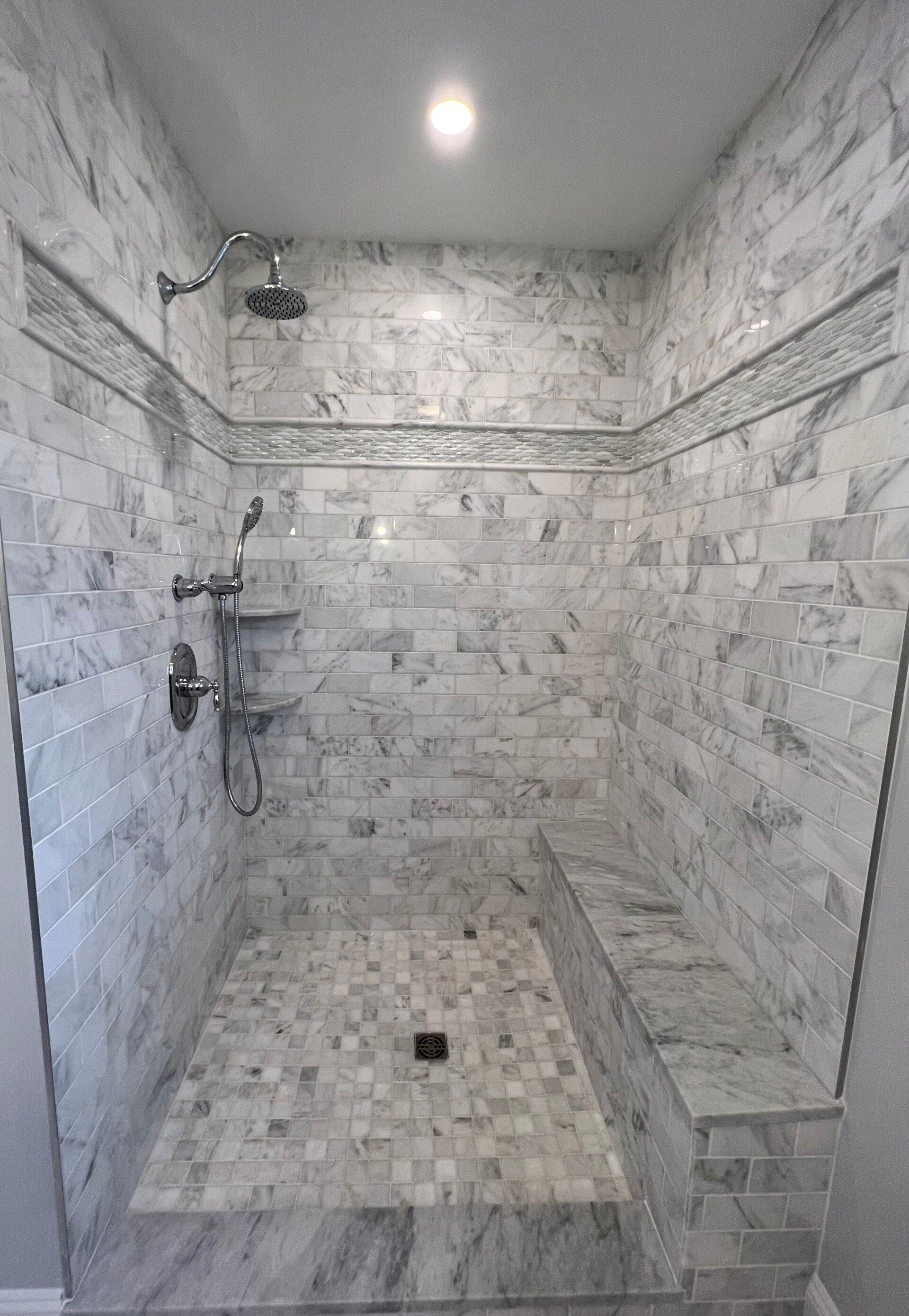 A bathroom with a walk in shower and a bench.