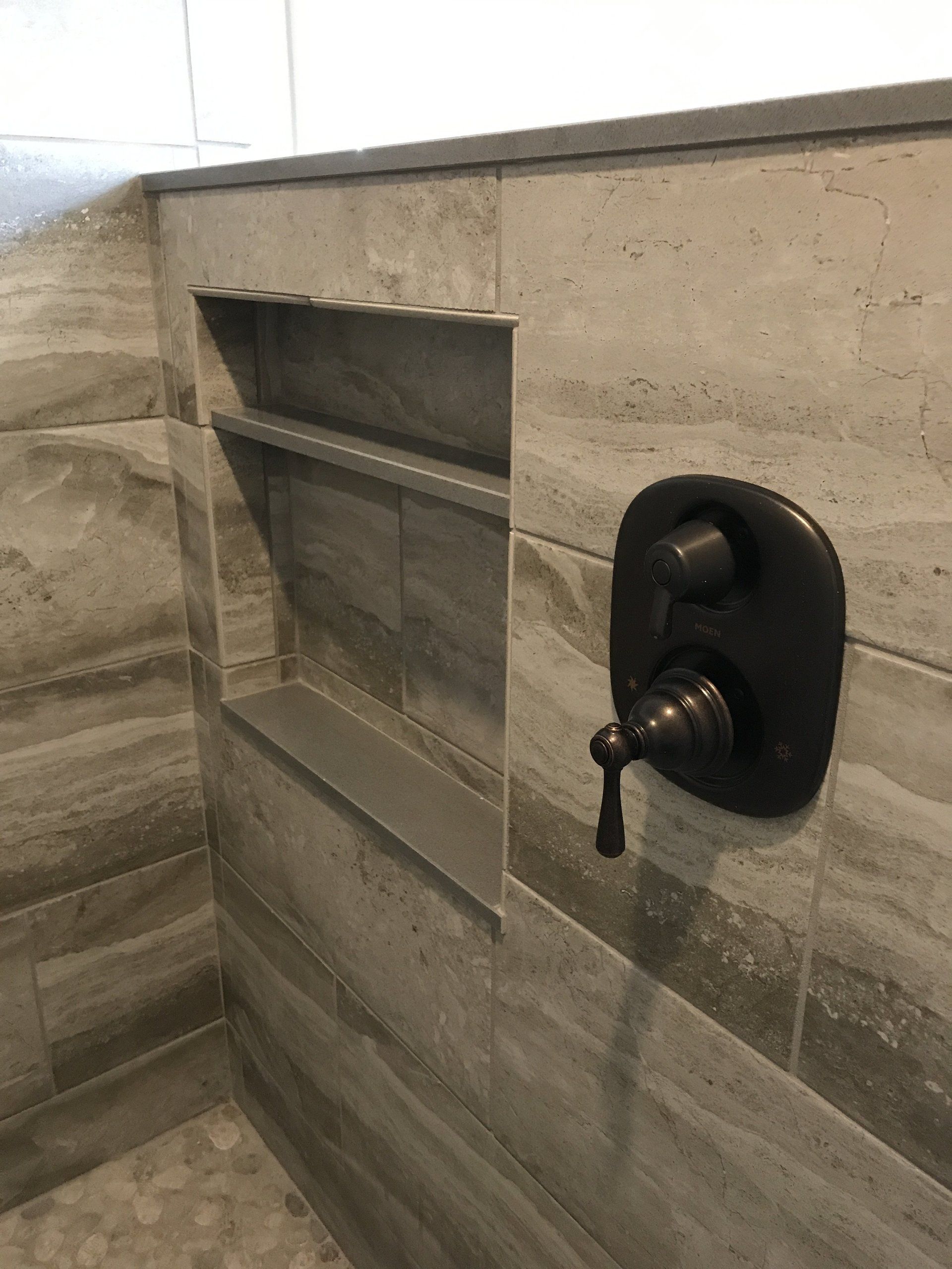 A shower with a built in shelf and a shower head.