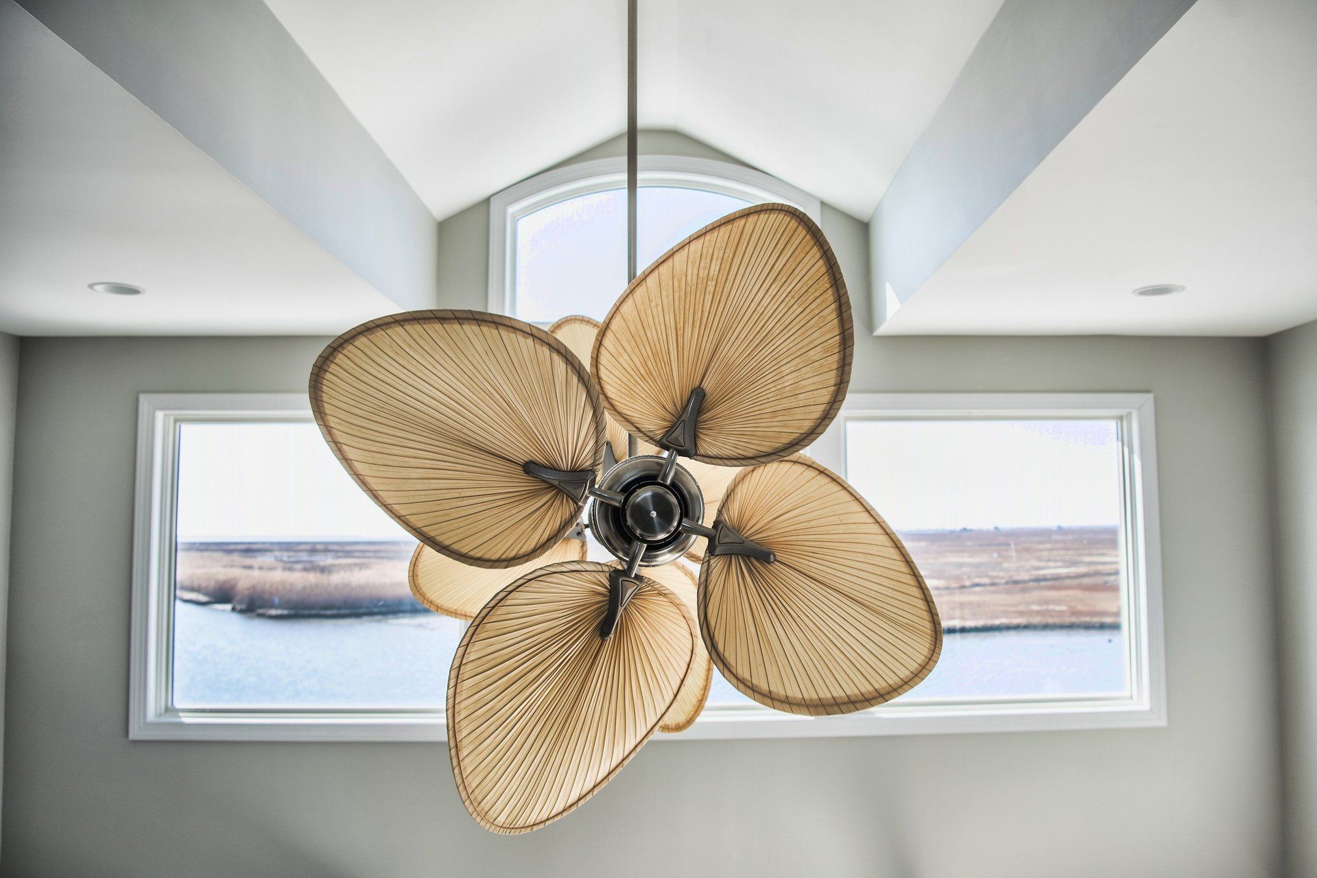 A ceiling fan is hanging from the ceiling in front of a window overlooking a body of water.