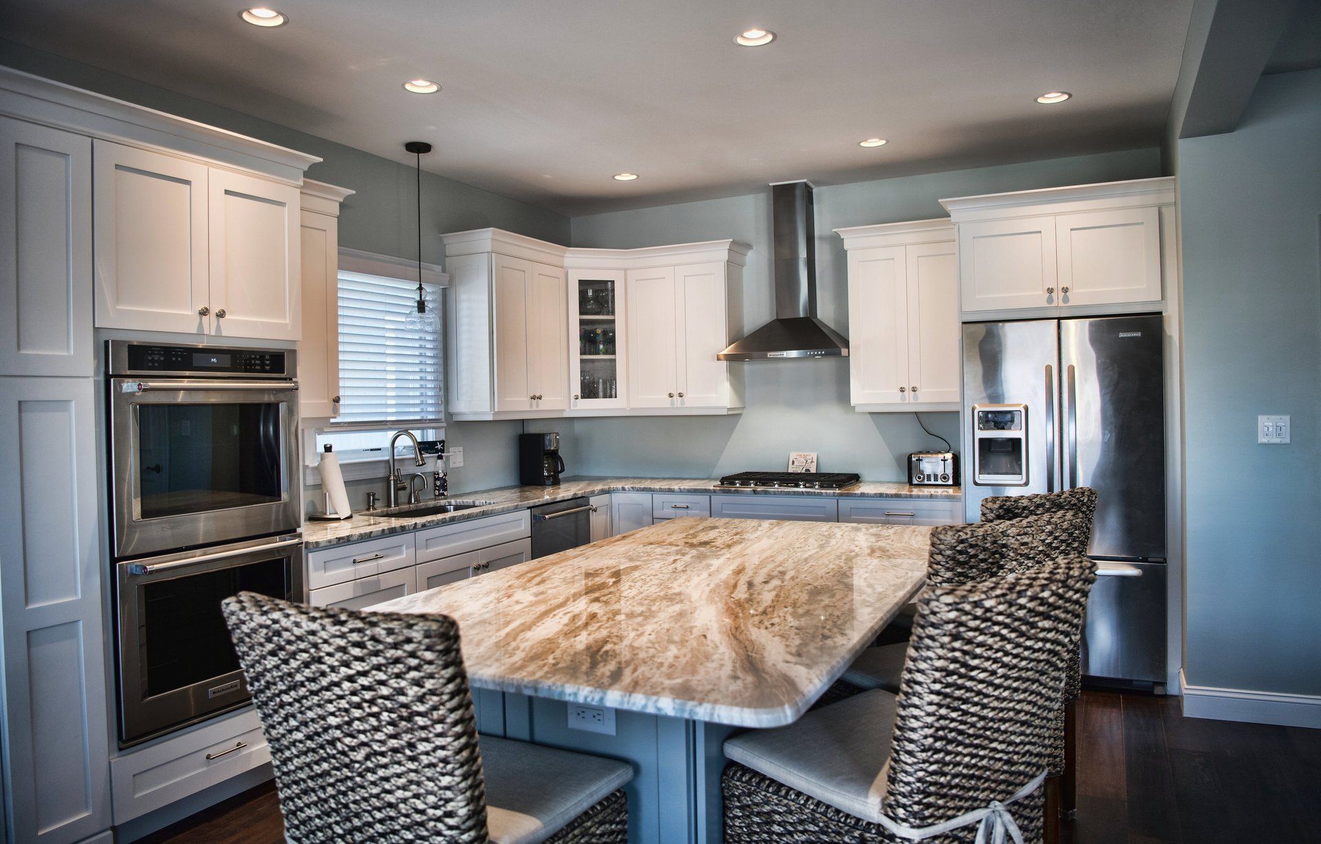 A kitchen with white cabinets , stainless steel appliances , a large island and wicker chairs.