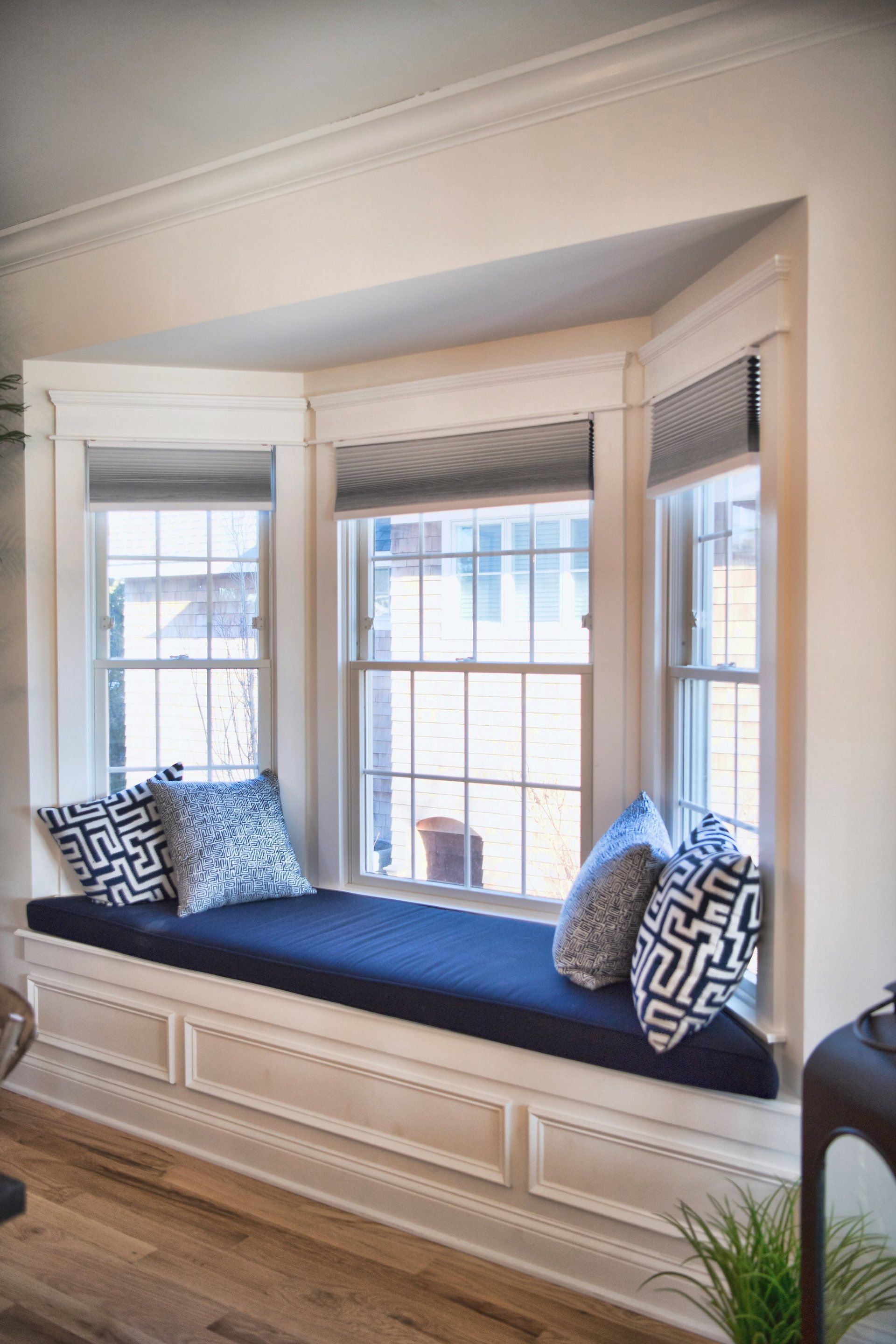 A window seat with a blue cushion and pillows in a living room.
