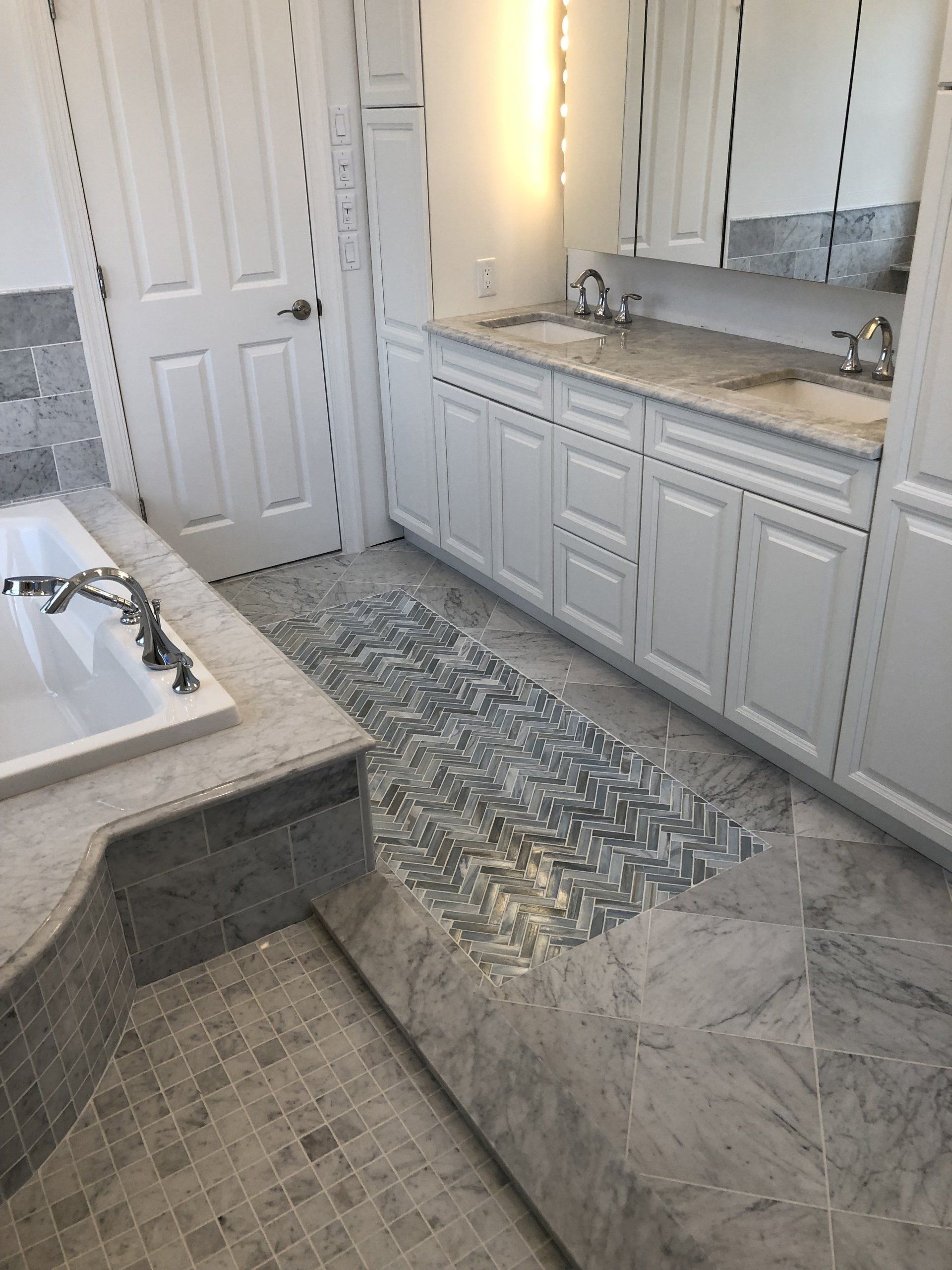 A bathroom with white cabinets , a bathtub , a sink and a mirror.