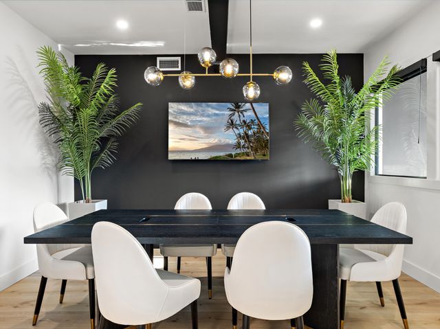 Modern meeting room with black accent wall, TV, and large table surrounded by white chairs.