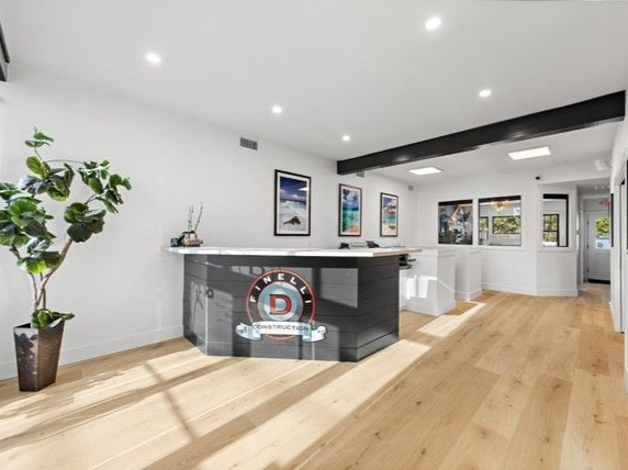 Reception area with a black and white desk, hardwood floors, and potted plant. 