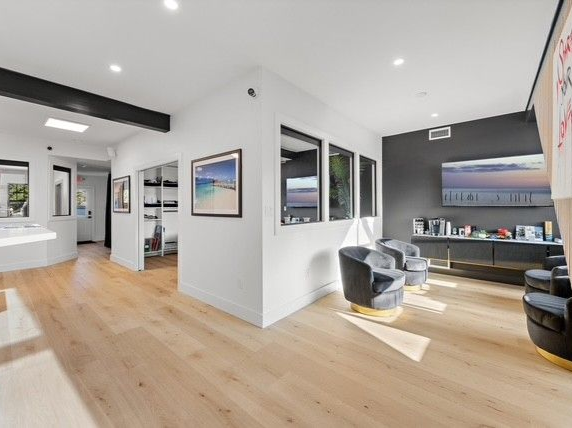 Bright living room with light wood floors, white walls, and dark accent wall with a television. 