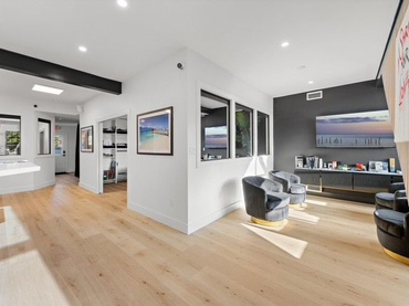 Bright living room with light wood floors, white walls, and dark accent wall with a television. 