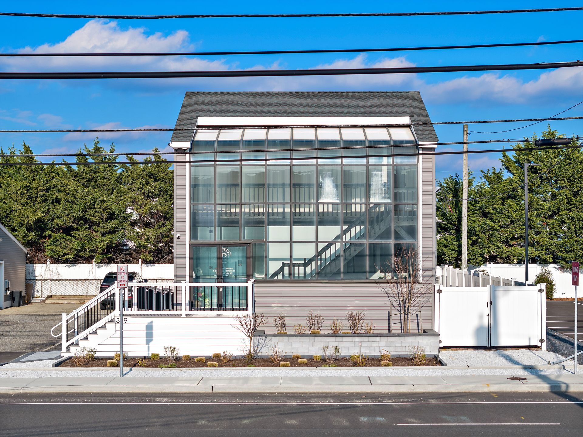 Modern building with glass front and white deck. Sidewalk, blue sky, and power lines.