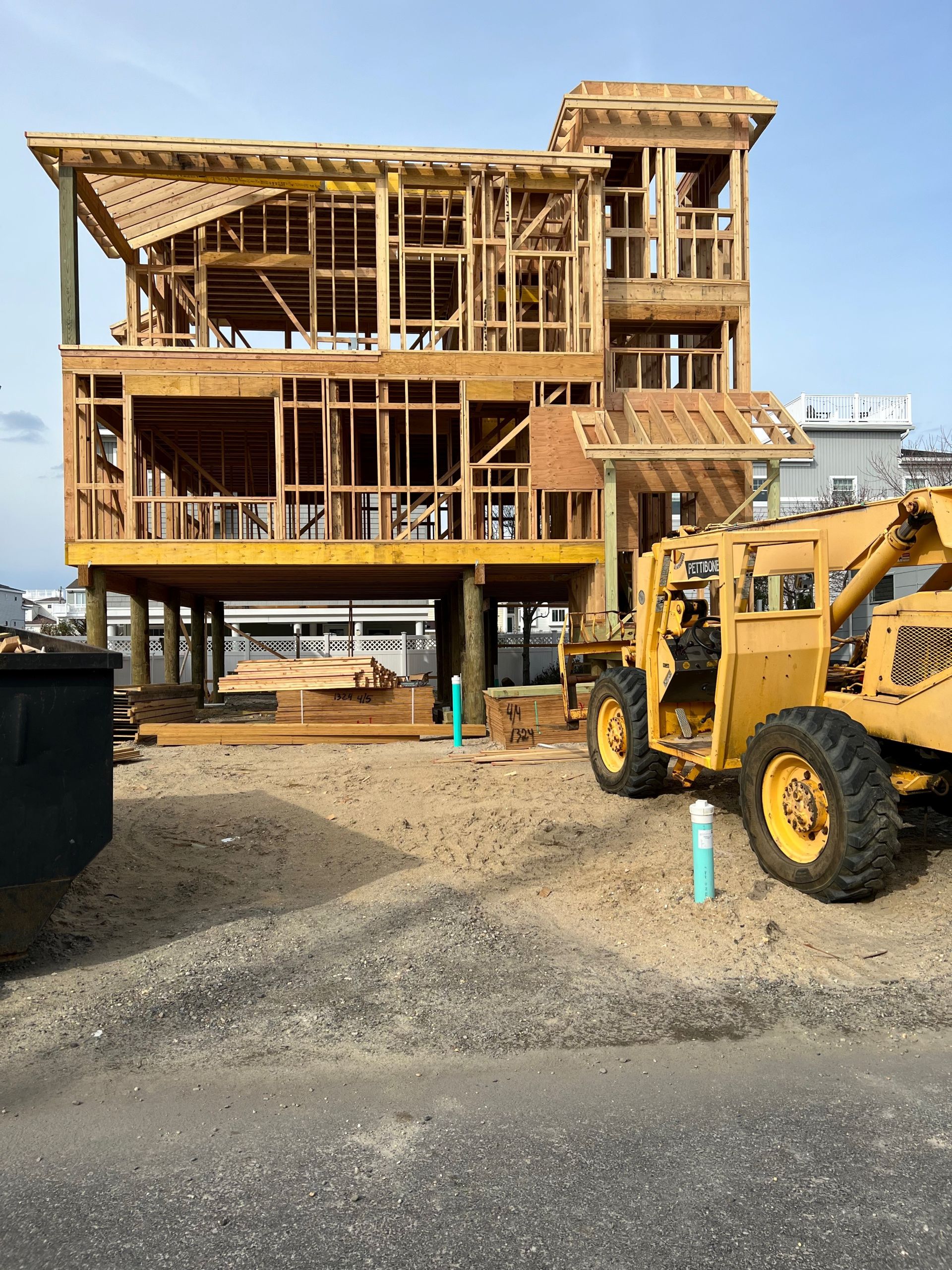 A yellow forklift is parked in front of a house under construction