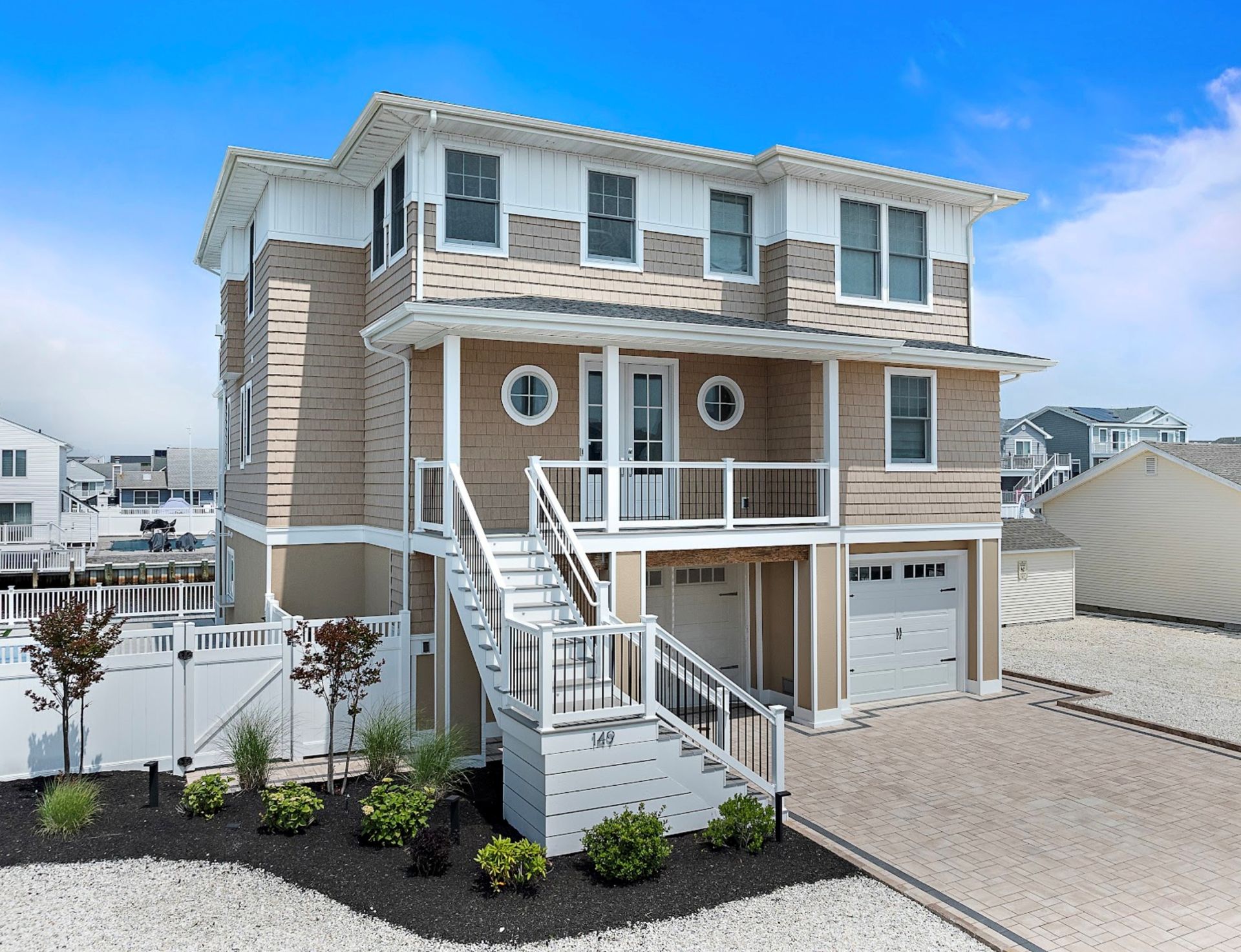 Two-story beach house with stairs, light brown and white exterior, and garage, on a sunny day.