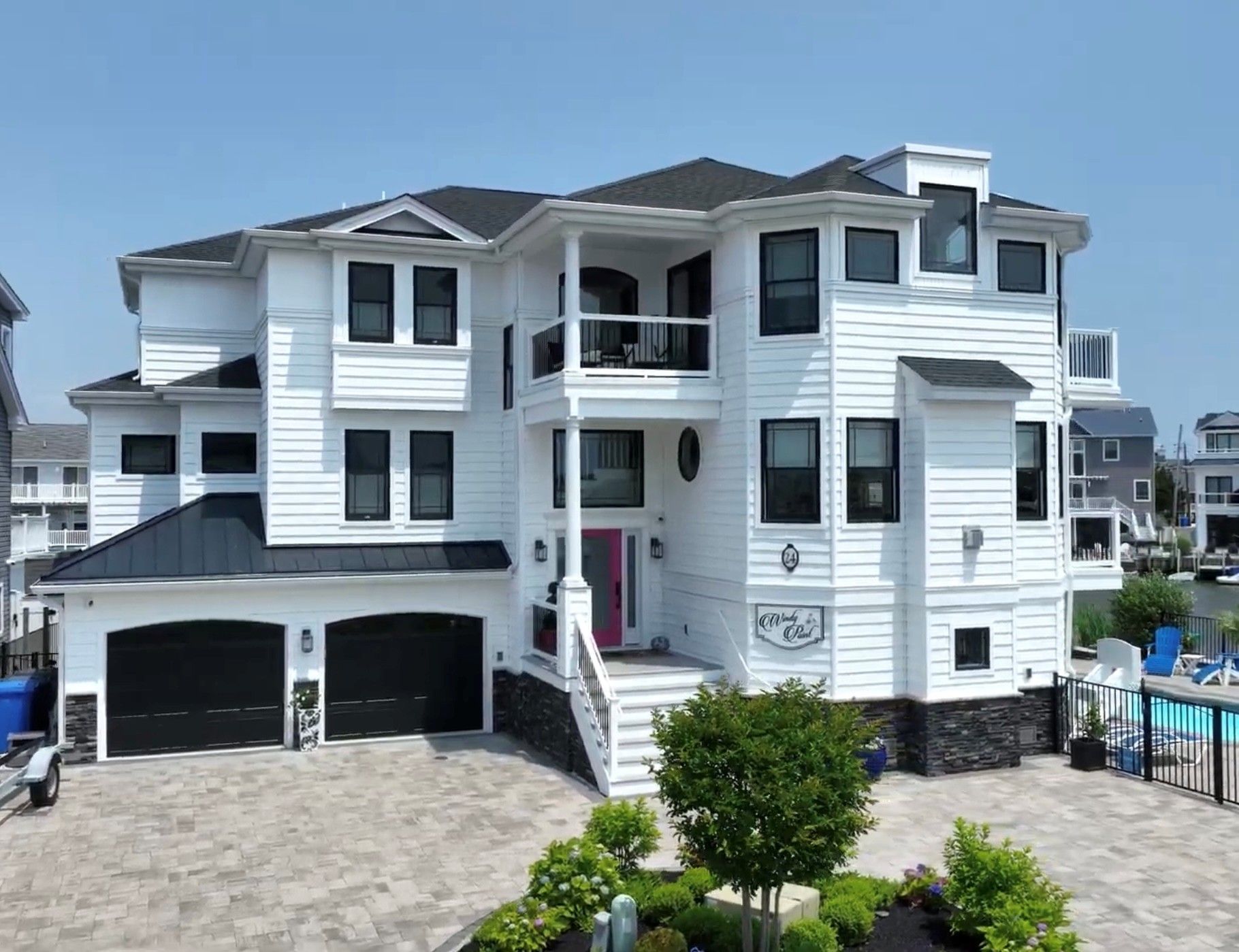 White beach house with black trim, pink door, and two-car garage, exterior view.