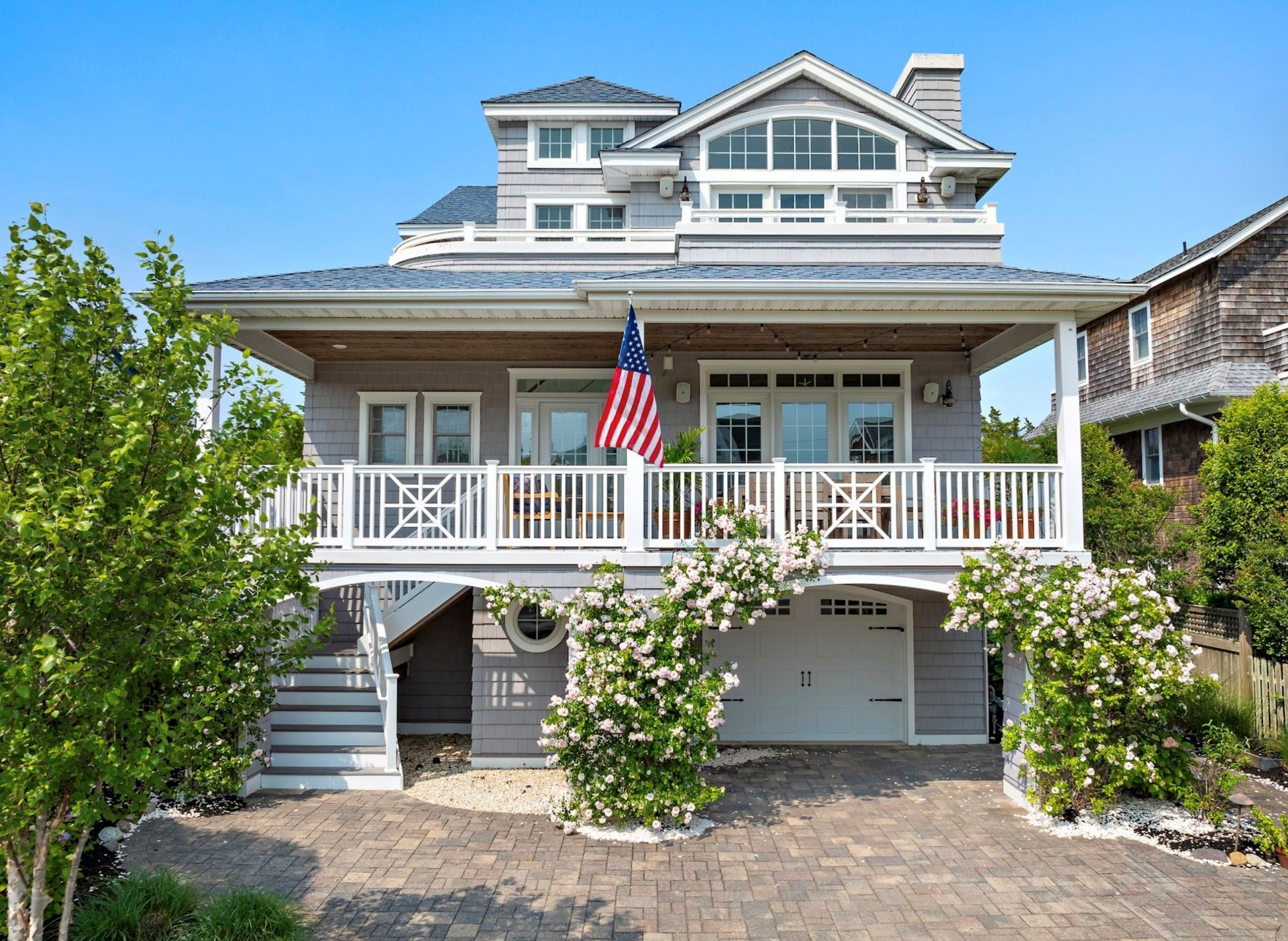 Gray beach house with a porch, American flag, and flowering vines.