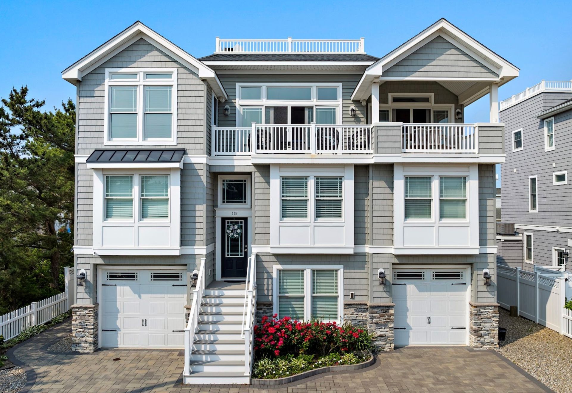 Gray beach house with white trim, multiple levels, balconies, and stone accents.