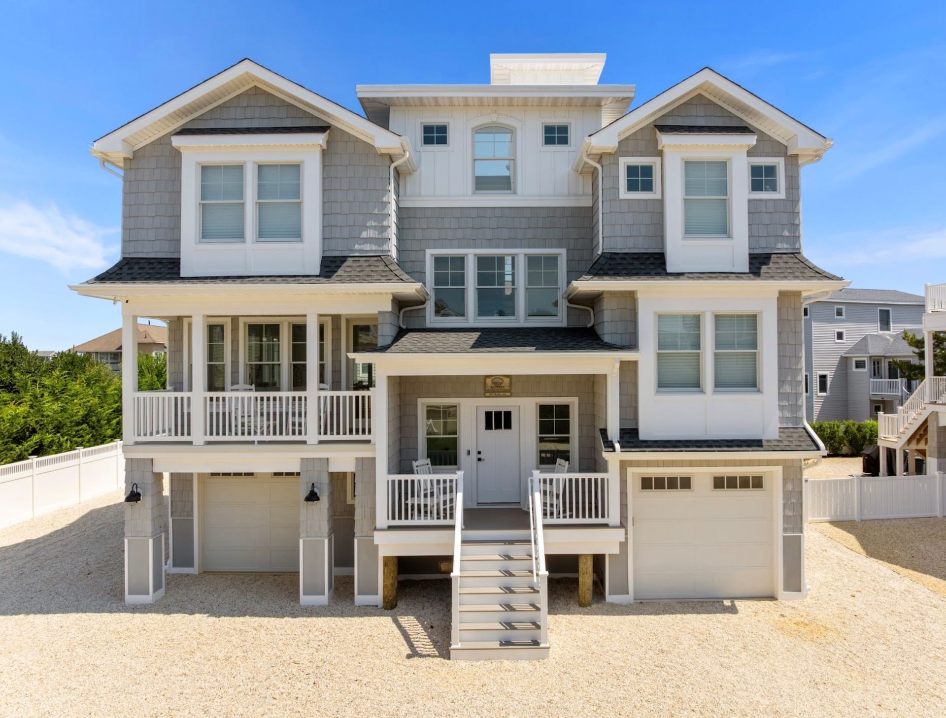Gray and white beach house with a white door and garage, standing on sand.