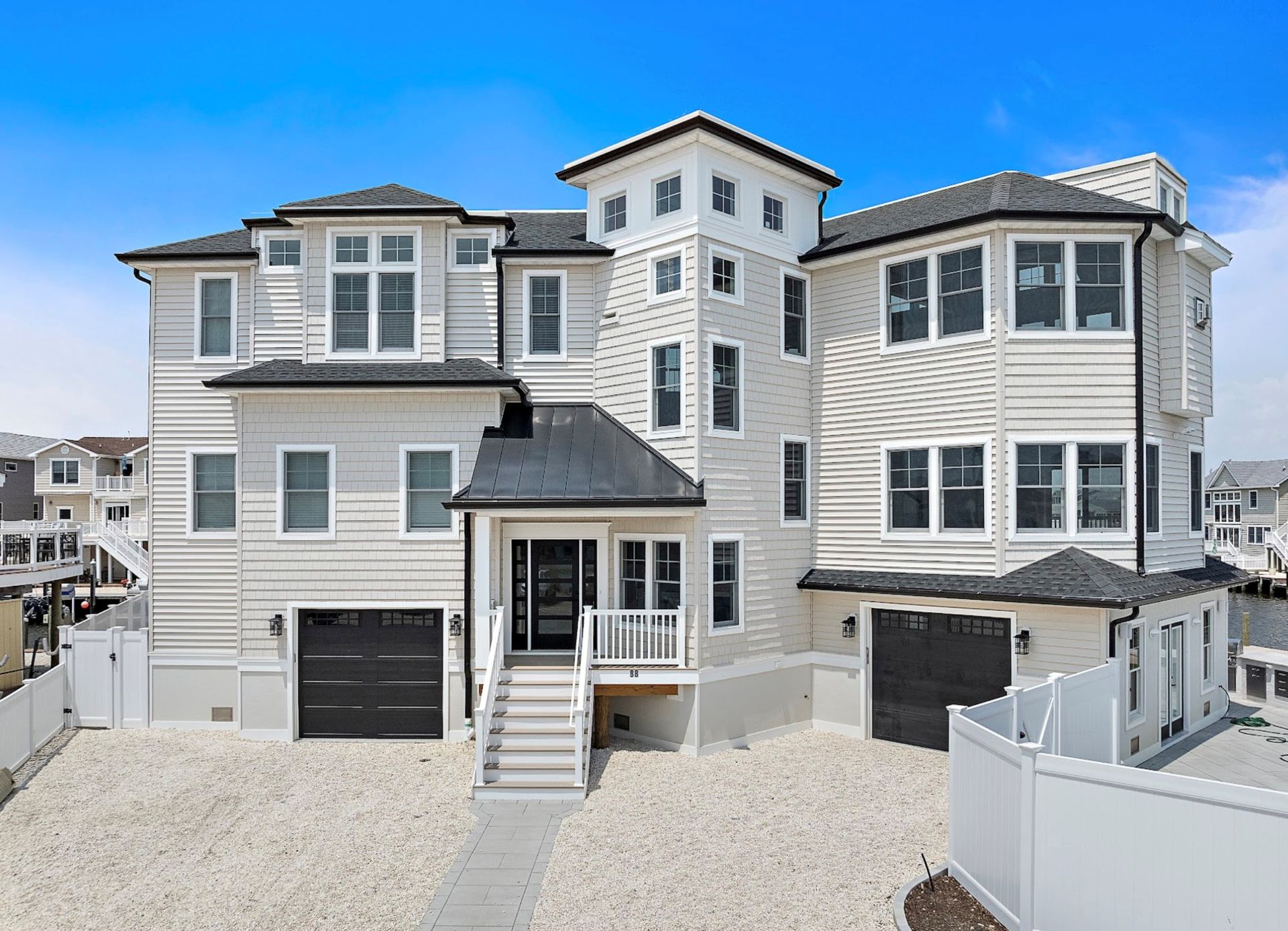 Beach house with light siding, dark garage doors, and a stone driveway.