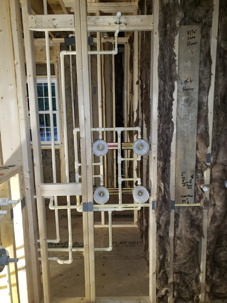 Exposed wood wall studs in a construction setting featuring complex white PVC plumbing pipes and valves for a shower.
