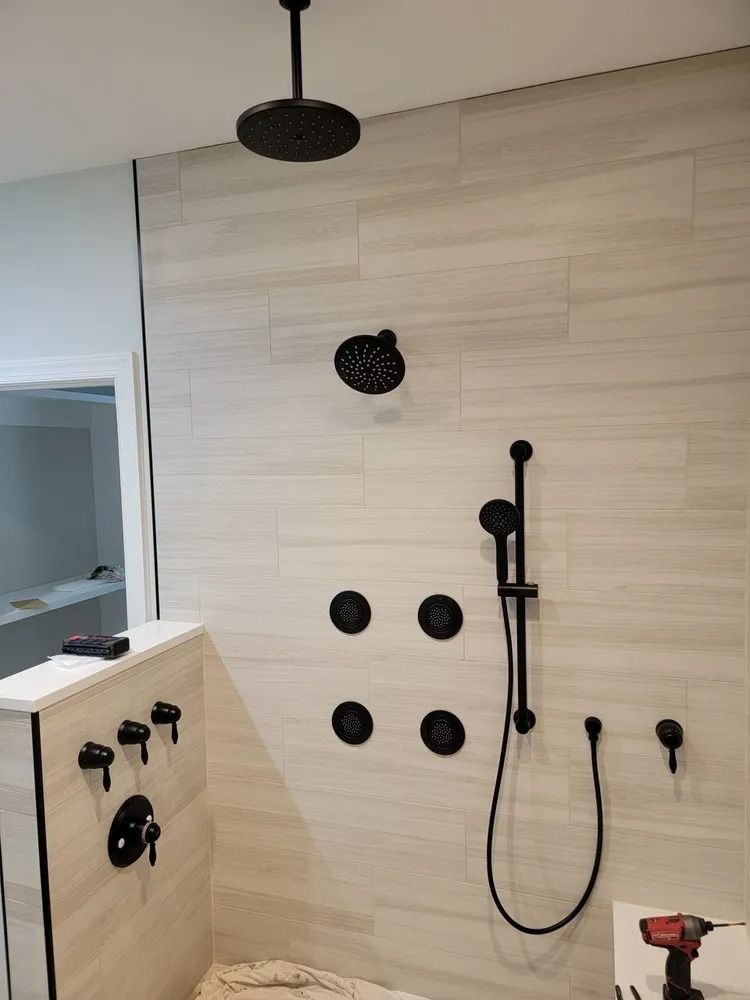 A modern shower installation featuring a rainfall head, wall jets, and a handheld sprayer with matte black fixtures.