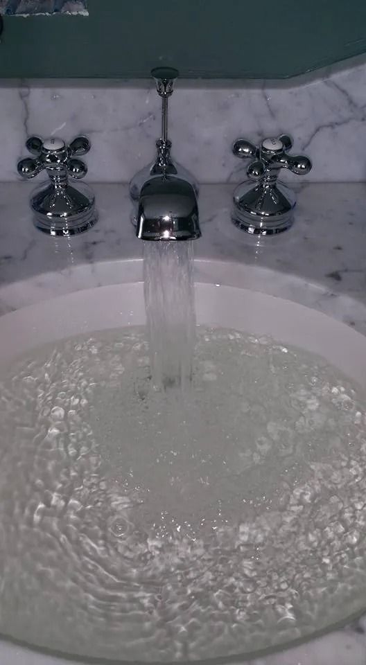 Water flows from a chrome bathroom faucet into a marble sink bowl.