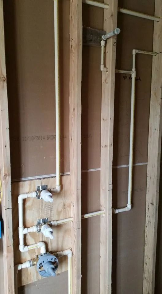 Plumbing pipes and valve controls for a shower system installed on unfinished wooden wall studs.