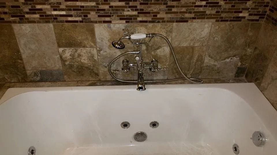 A white jetted bathtub featuring a chrome faucet and handheld sprayer against a brown tiled wall.