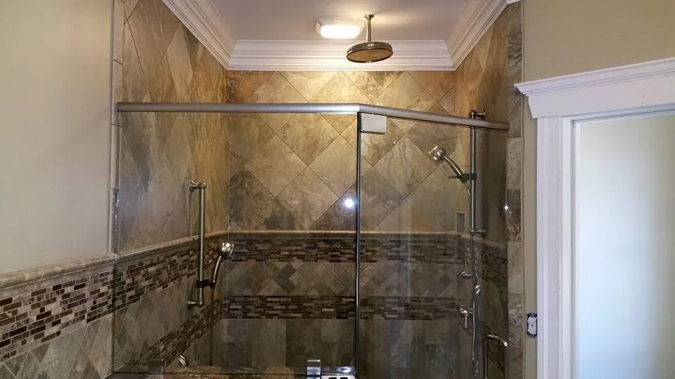 A walk-in shower with beige, diamond-patterned tile, a glass door, a rain showerhead, and a brown mosaic border accent.