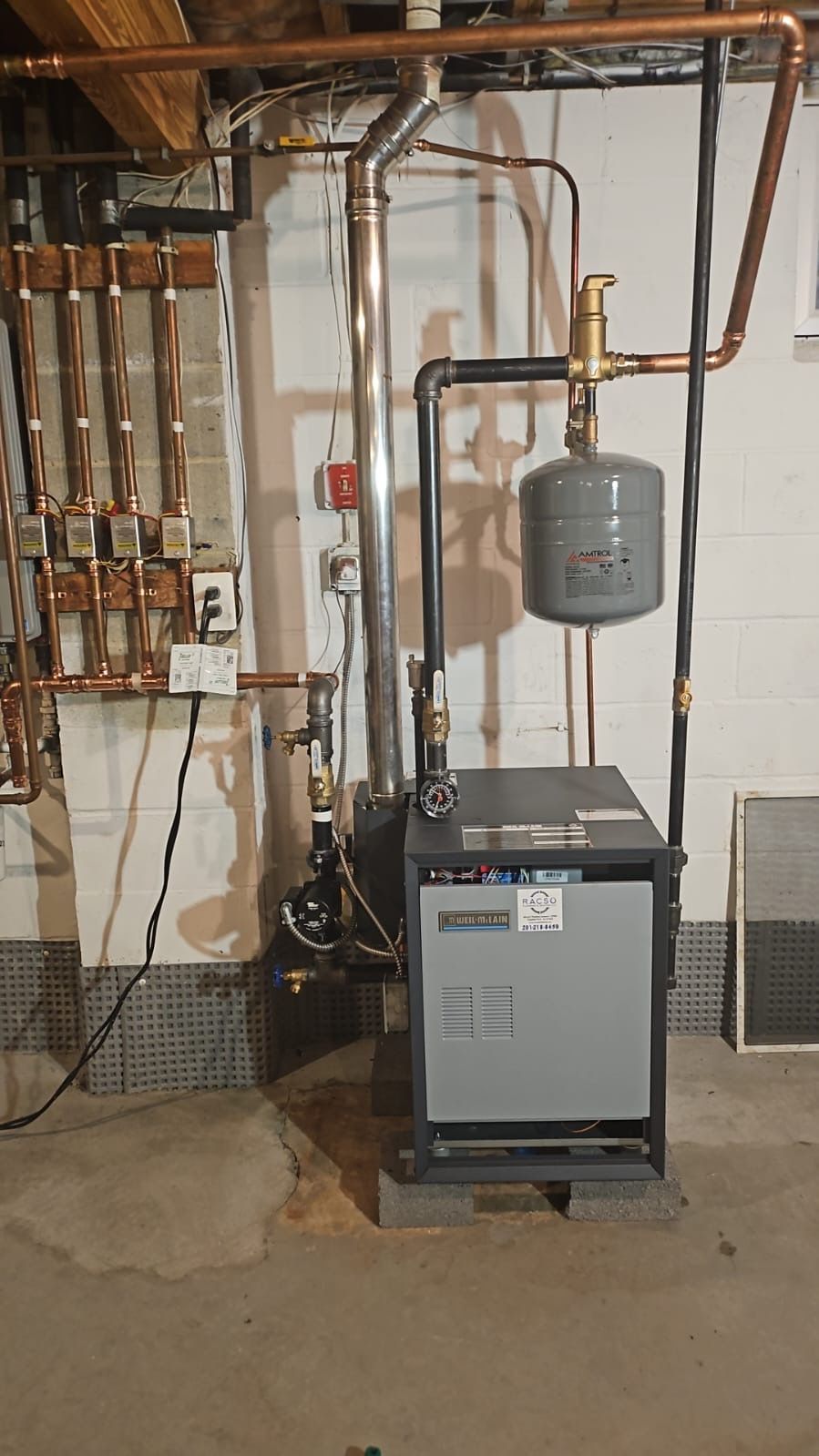 A boiler in a basement next to pipes