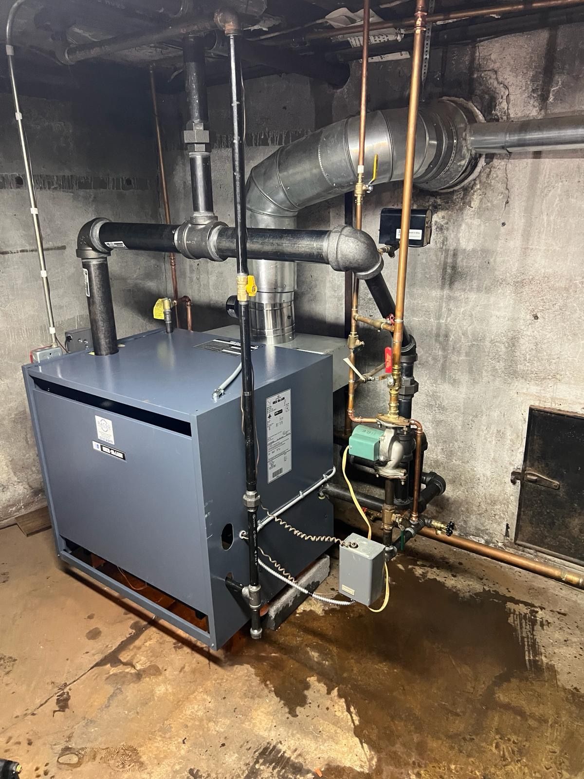 A boiler in a basement next to several pipes