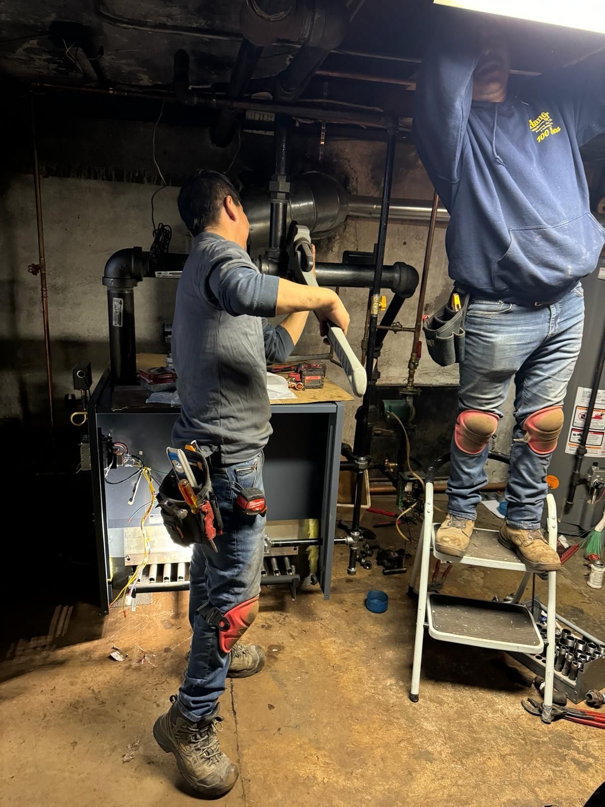 Two men are working on a pipe in a basement