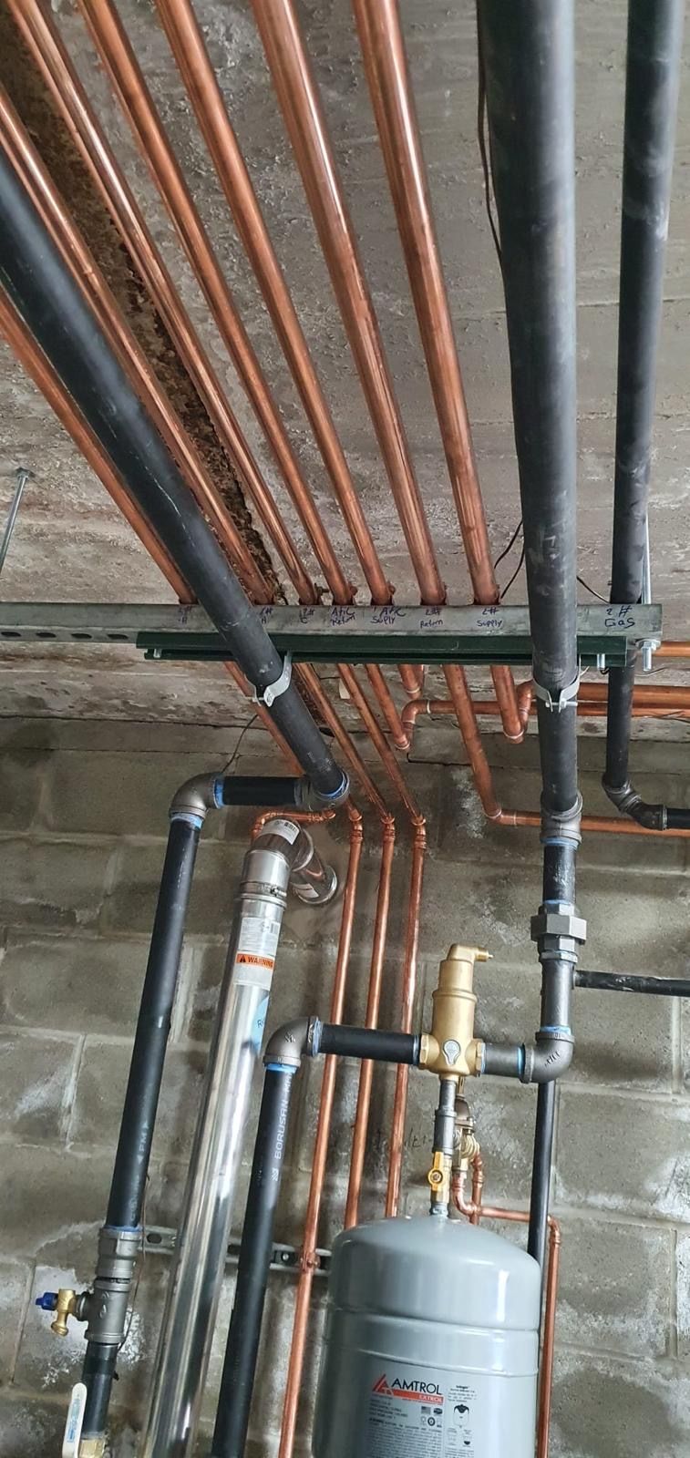 A bunch of copper pipes hanging from the ceiling of a building with a water heater below them