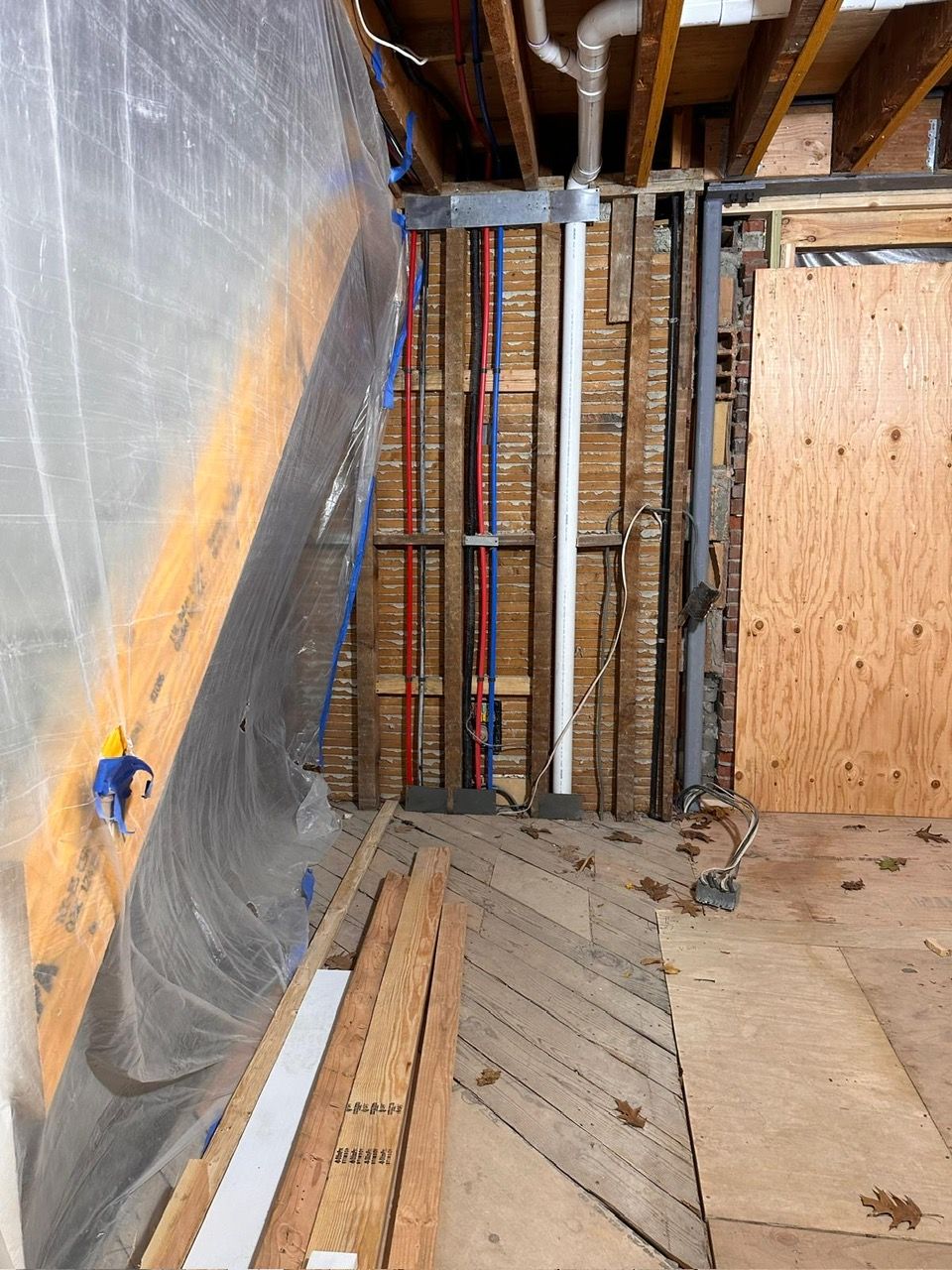 A room with wooden walls. plumbing pipes, and a plastic sheet on the wall