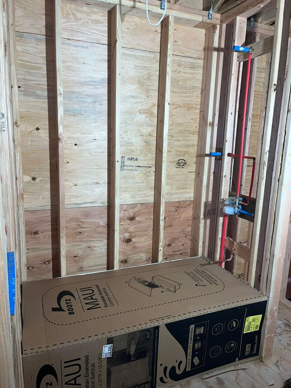 A bathtub box in the middle of a wooden room with installed plumbing pipes