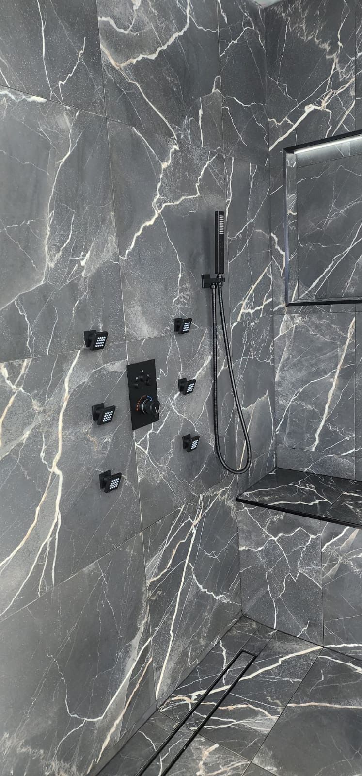 A bathroom with marble tiles and walls and a shower head