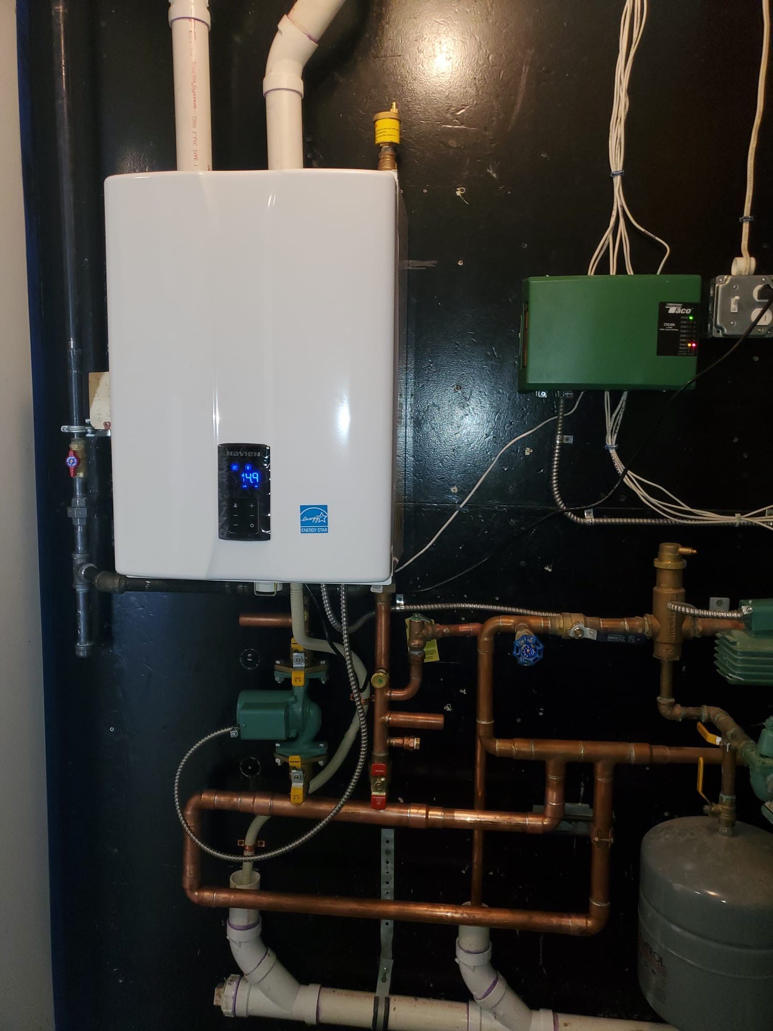 A white water heater on a wall next to copper pipes