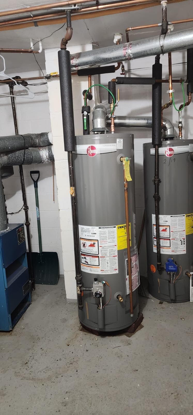 Two water heaters are sitting next to each other in a basement
