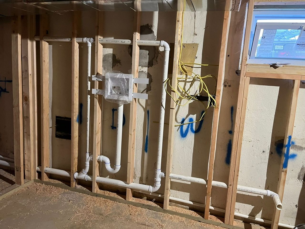 A room under construction with a window and pipes on the wall