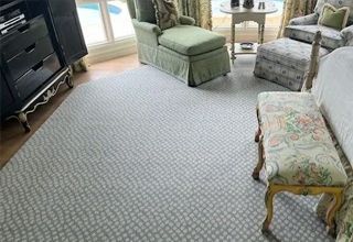 A bedroom with a blue patterned rug, a green chaise lounge, floral upholstered chair, and a black dresser.