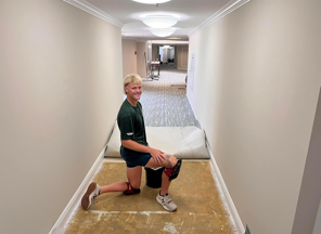 A man is kneeling down in a hallway with a bucket.