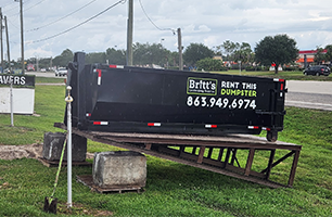 A dumpster is sitting on top of a wooden ramp in the grass.