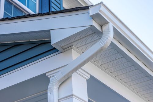 Close-up of a white house gutter and downspout under a blue metal roof