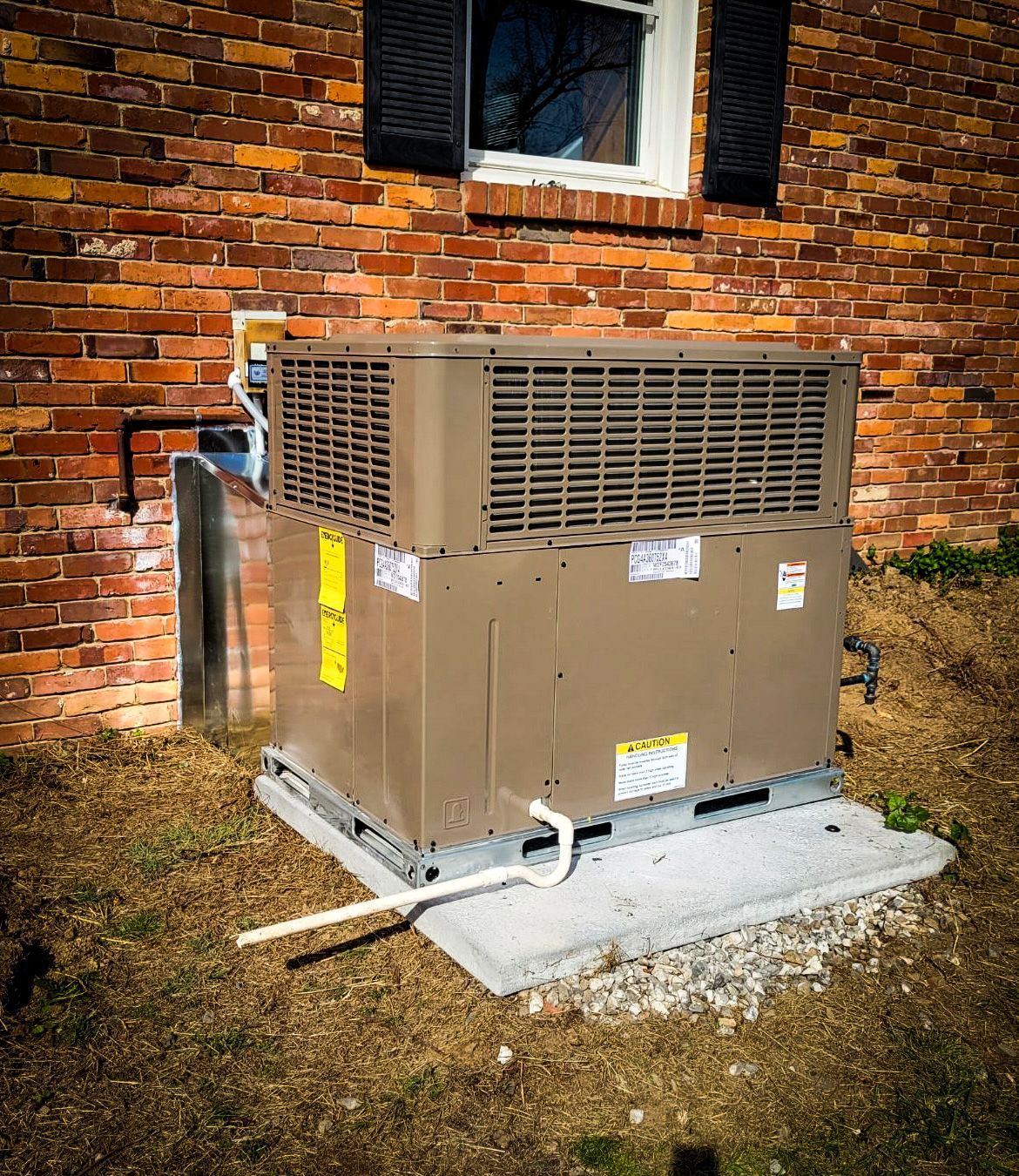 Brown HVAC unit outside a brick building with a window and closed shutters.