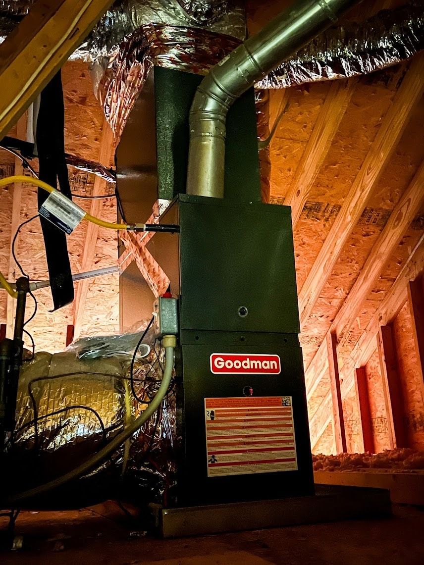 Black Goodman furnace in an unfinished attic, with ductwork and exposed wood beams.