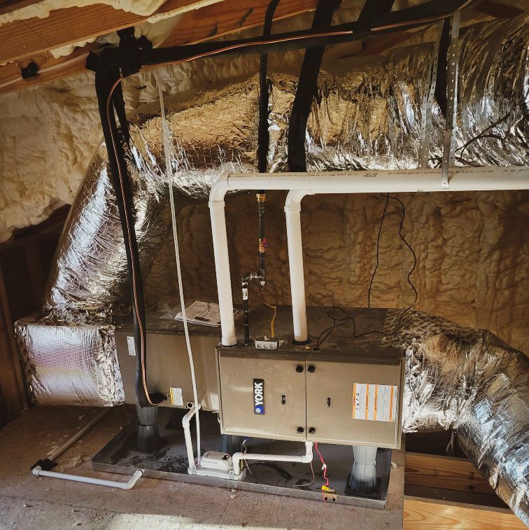 HVAC unit installed in an attic. Silver ductwork and insulation are visible. White PVC piping and black gas lines.