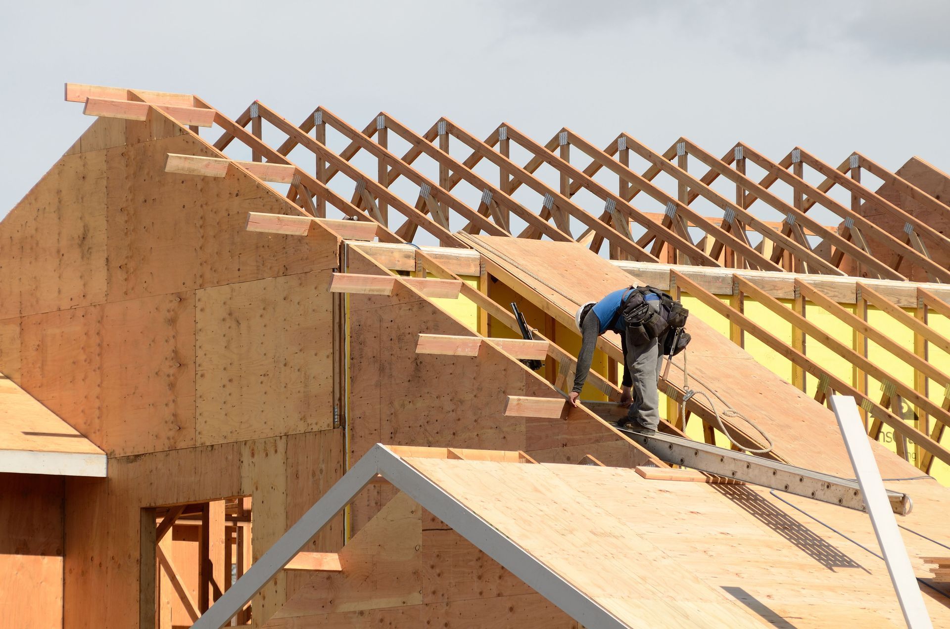Construction worker on a roof framing a house with exposed wooden trusses